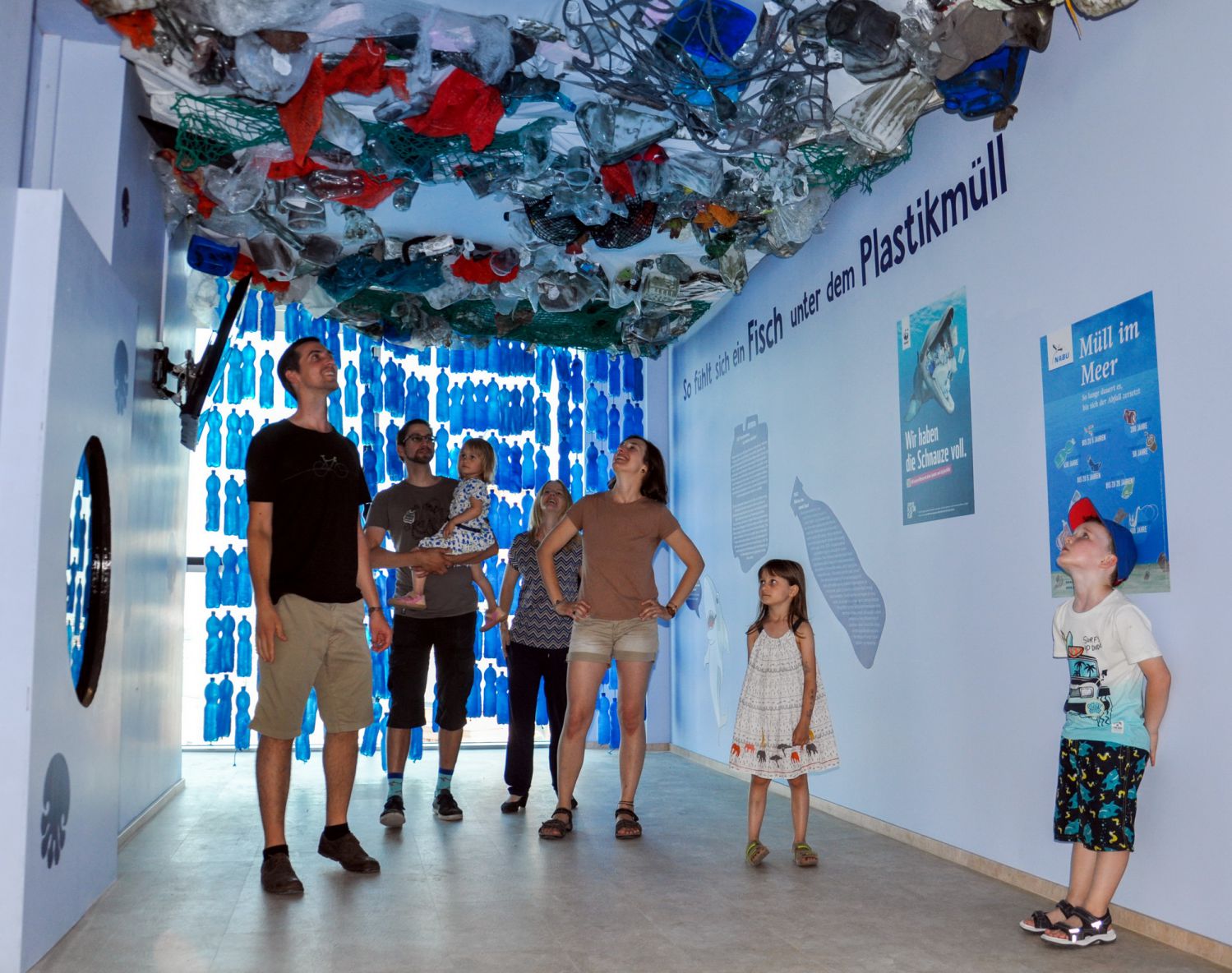 Besucher der Ausstellung blicken von unten auf den Müllstrudel an der Decke